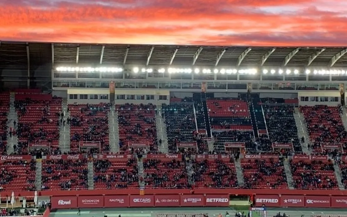 Grada del estadio del RCD Mallorca al atardecer, con el cielo rojo y los focos encendidos.